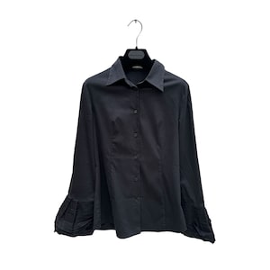 May include: A black button-down shirt with long sleeves and a classic collar. The sleeves feature pleated detailing at the cuffs. The shirt is hanging on a black hanger against a white background.
