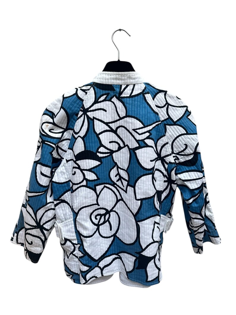 Peut inclure: Une veste matelass&eacute;e bleu et blanc avec un imprim&eacute; floral. La veste a un col montant et des manches longues.