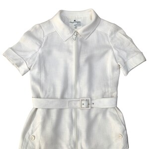 May include: A white linen zip-up shirt with short sleeves and a belt. The shirt has a collar and two buttons on the bottom. The label reads "Courr&egrave;ges Paris".