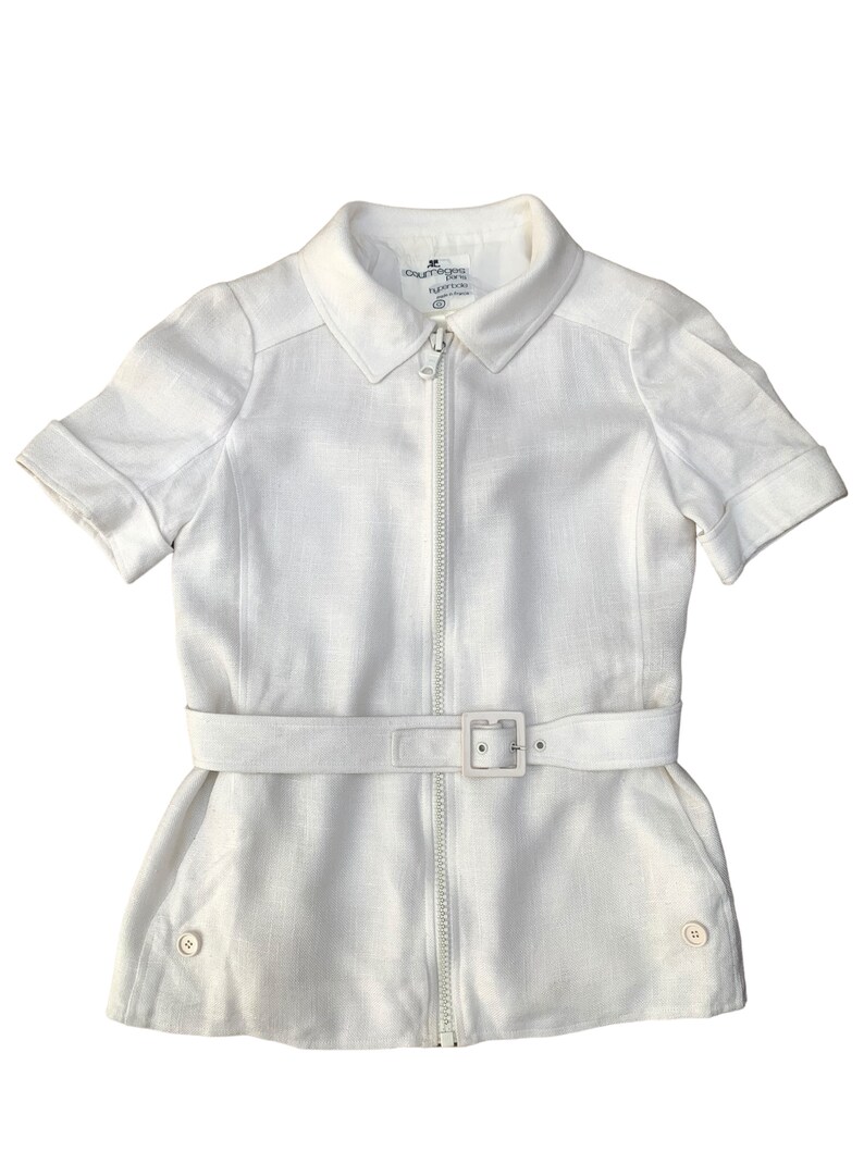 May include: A white linen zip-up shirt with short sleeves and a belt. The shirt has a collar and two buttons on the bottom. The label reads "Courr&egrave;ges Paris".