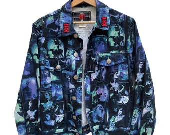 May include: A dark denim jacket featuring an all-over print of blue and purple human figures in various poses. The jacket has a collared neckline, long sleeves with buttoned cuffs, two chest pockets with button closures, and a front button closure.