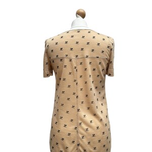 May include: A peach-colored short-sleeved dress with a black and white print of a repeated pattern. The dress has a round neckline and a slightly flared skirt.