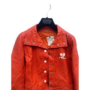 May include: A bright orange leather jacket with a white logo that says "Courr&egrave;ges Paris". The jacket has a high collar and a button closure.
