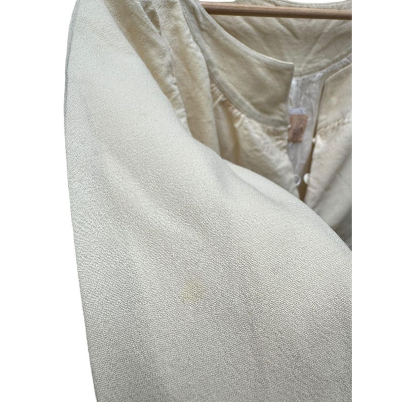 Pode incluir: Uma blusa de manga comprida de cor creme com decote redondo e fecho de bot&otilde;es. A blusa &eacute; feita de um tecido macio e texturizado.