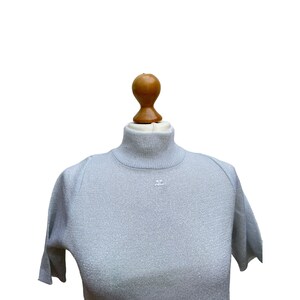 Peut inclure: Un pull gris clair à col roulé à manches courtes avec un petit logo blanc sur le devant.
