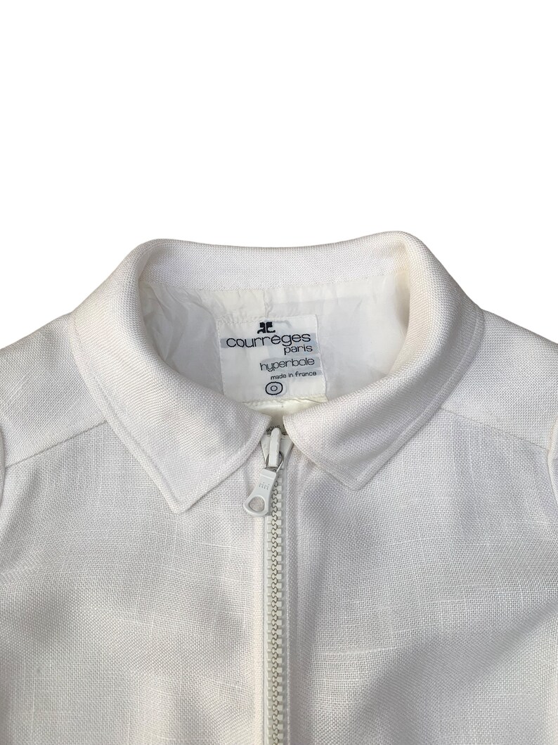 May include: White linen jacket with a zipper closure and a label that reads "Courr&egrave;ges Paris Hyperbole made in France".