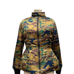 May include: A camouflage-patterned jacket with a high collar and a full-length zipper. The jacket features a mix of green, blue, and brown hues on a gold background. The cuffs are black. The jacket is displayed on a vintage dress form.
