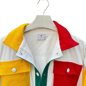 Puede incluir: Una chaqueta blanca con un dise&ntilde;o de patchwork colorido. La chaqueta tiene un cuello verde, paneles amarillos y rojos y un cierre de botones blancos. La etiqueta dice "Courr&egrave;ges Paris".