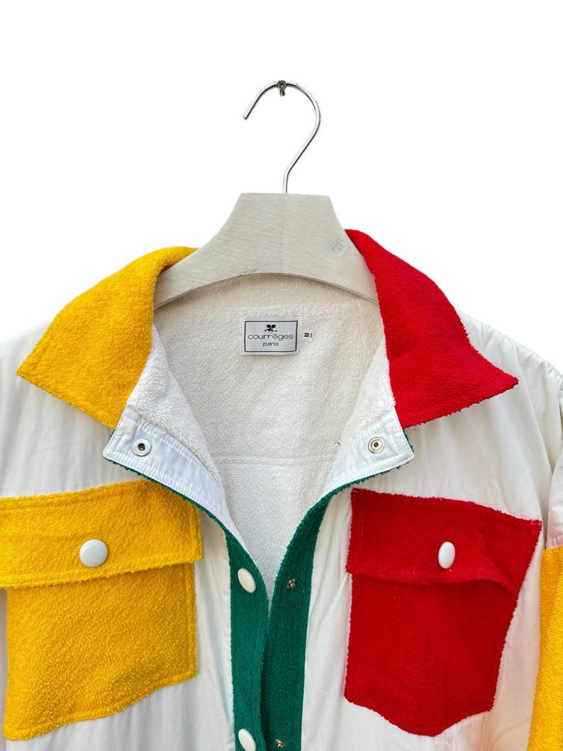 Puede incluir: Una chaqueta blanca con un dise&ntilde;o de patchwork colorido. La chaqueta tiene un cuello verde, paneles amarillos y rojos y un cierre de botones blancos. La etiqueta dice "Courr&egrave;ges Paris".