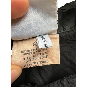 May include: A close-up of a black silk garment tag with white text. The tag reads "Nettoyer par 1, Repasser a fer doux, Tissu/Material 100% Soie/Silk, Tissu/Material 100% Soie/Silk" and "Made in Spain".