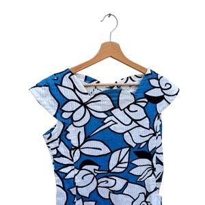 Puede incluir: Un vestido de estampado floral azul y blanco con mangas cortas colgado de una percha de madera. El vestido tiene cuello en V y un corte holgado.