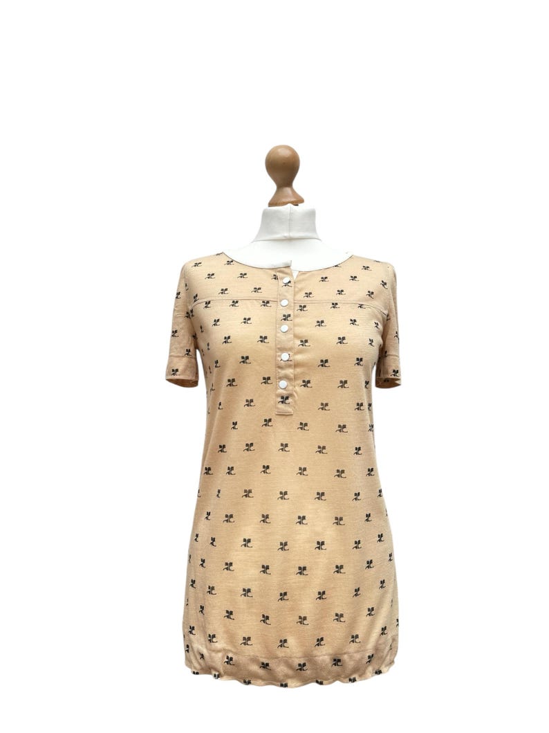 May include: A beige short-sleeved dress with a button-up front and a small black floral print.