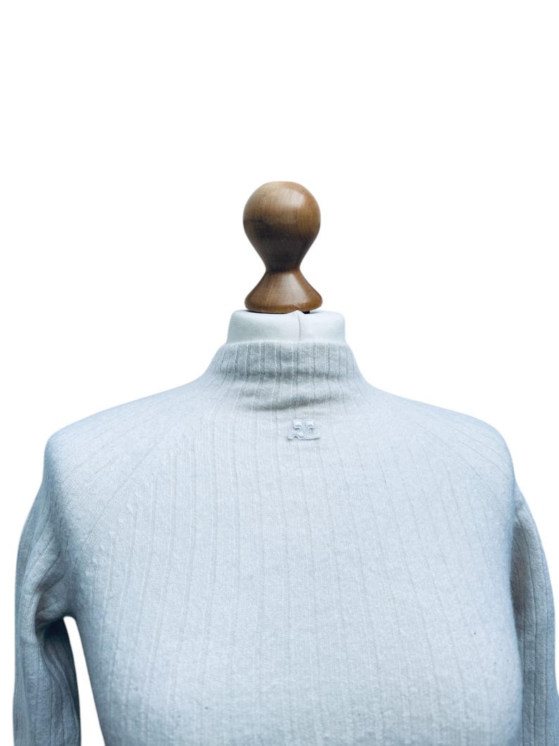 May include: A light blue ribbed turtleneck sweater with a small white button on the front.