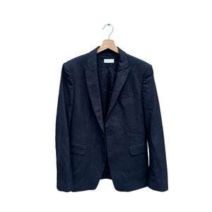 May include: A dark navy blue blazer with a two-button closure, notched lapels, and two front pockets. The blazer is hanging on a wooden hanger against a white background. The blazer is a classic style.
