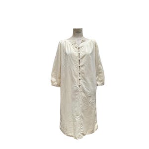Pode incluir: Um vestido comprido de linho branco-queimado com decote redondo e fecho de bot&otilde;es na frente. O vestido tem um caimento solto e uma cintura ligeiramente franzida.