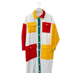 Puede incluir: Una camisa blanca de manga larga con un frente abotonado verde. La camisa tiene grandes cuadrados rojos, amarillos y verdes cosidos en la parte delantera y las mangas.