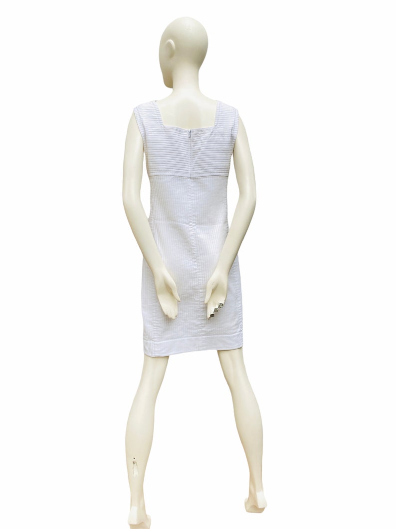 May include: A white sleeveless dress with thin vertical stripes. The dress has a square neckline and a zipper closure in the back.