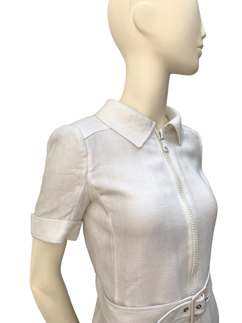 May include: White linen dress with a zipper closure and a belt. The dress has short sleeves and a collared neckline.
