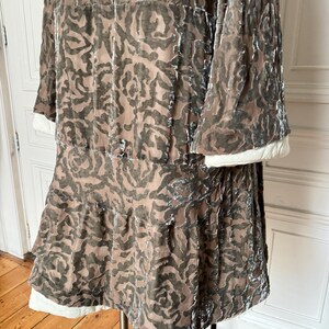 Puede incluir: Vestido vintage en tonos marr&oacute;n y gris con estampado floral. Mangas largas con pu&ntilde;os blancos y falda escalonada con ribete blanco. La tela parece terciopelo. El vestido se exhibe en un soporte.