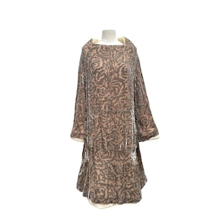 Puede incluir: Vestido de estilo vintage en una paleta de colores suaves y apagados. El vestido presenta un estampado floral en tonos marrones y beige, con una falda escalonada y mangas anchas. El escote y los pu&ntilde;os est&aacute;n ribeteados con una tela color crema.