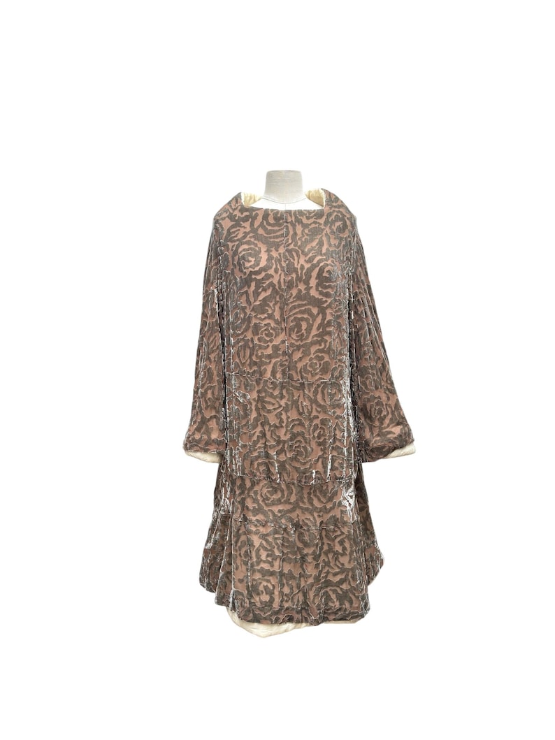 Puede incluir: Vestido de estilo vintage en una paleta de colores suaves y apagados. El vestido presenta un estampado floral en tonos marrones y beige, con una falda escalonada y mangas anchas. El escote y los pu&ntilde;os est&aacute;n ribeteados con una tela color crema.