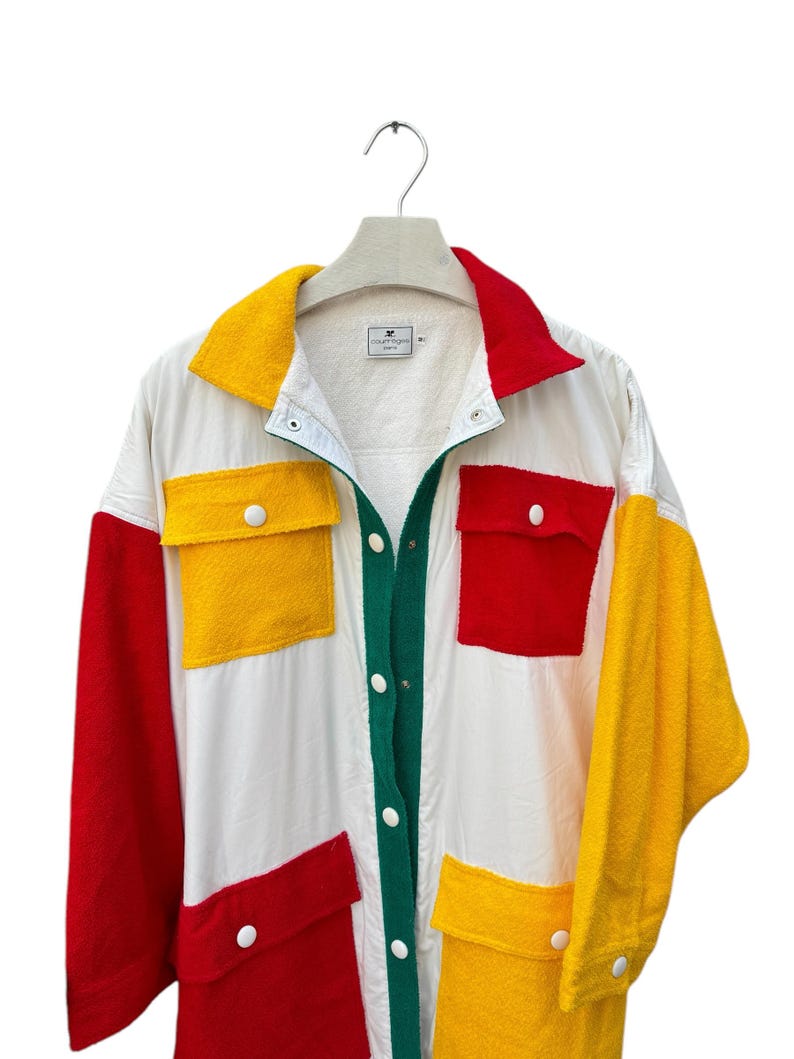 Puede incluir: Una camisa blanca de manga larga con botones con paneles rojos, amarillos y verdes. La camisa tiene bolsillos grandes en la parte delantera y un cuello de contraste.