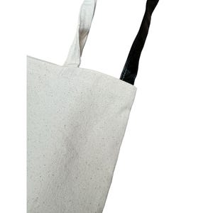 May include: A white canvas tote bag with black leather handles.