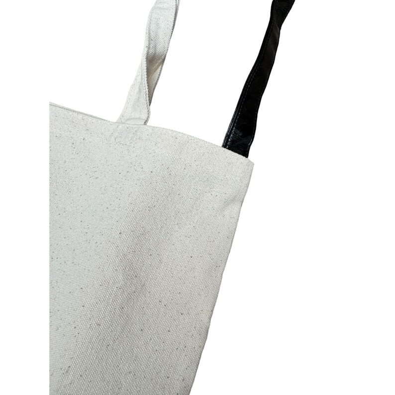 May include: A white canvas tote bag with black leather handles.