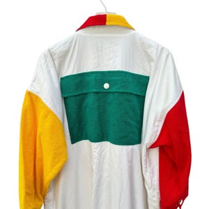 Puede incluir: Camisa blanca de manga larga con un dise&ntilde;o de bloques de color verde, amarillo y rojo. La camisa tiene un bolsillo de parche en la espalda y un cierre de bot&oacute;n.