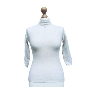 May include: A white ribbed sweater with a mock neck and three-quarter sleeves.