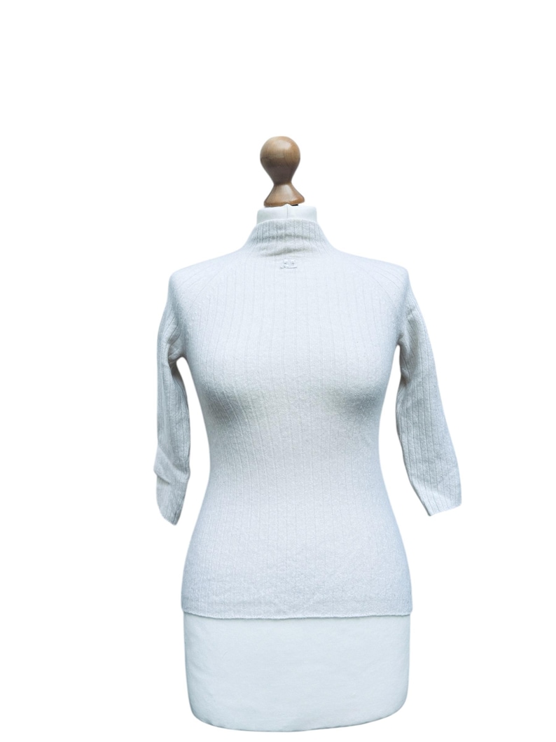May include: A white ribbed sweater with a mock neck and three-quarter sleeves.