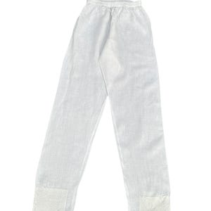 May include: White linen pants with an elastic waistband and decorative embroidered patches at the ankles. The pants are lightweight and appear to be breathable, suitable for warm weather. The fabric has a slightly textured appearance.