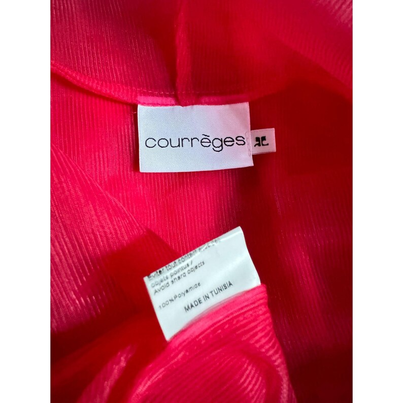 May include: Close-up of a bright pink garment with the brand label "courr&egrave;ges" visible. The label is white with black text. A second label reads "100% Polyamide" and "MADE IN TUNISIA". The fabric has a ribbed texture.