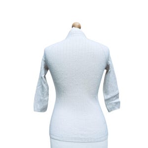 May include: A white ribbed sweater with long sleeves on a mannequin.