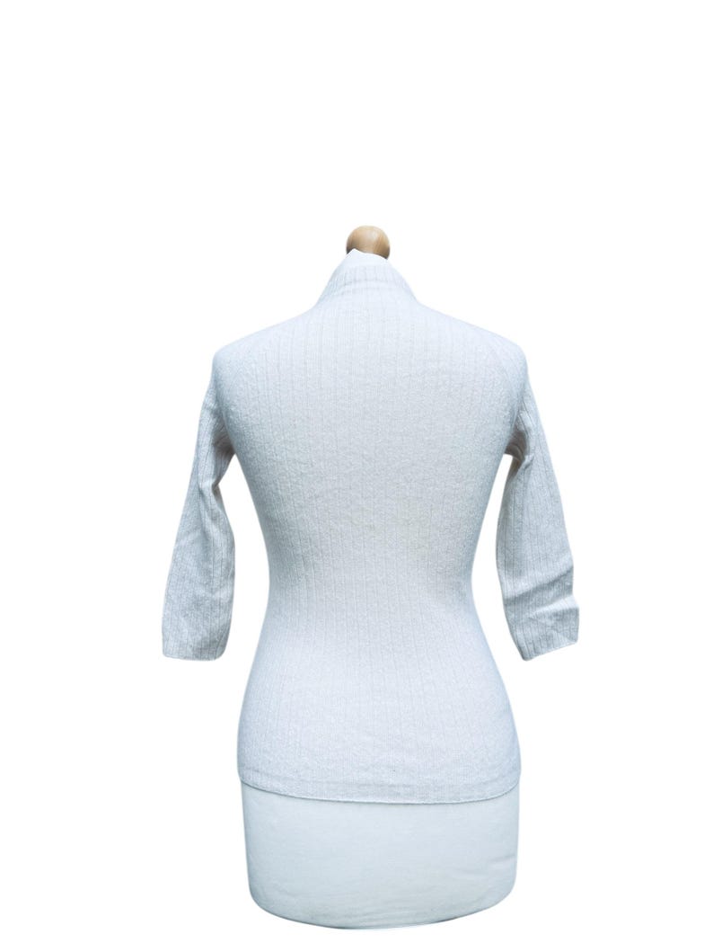 May include: A white ribbed sweater with long sleeves on a mannequin.