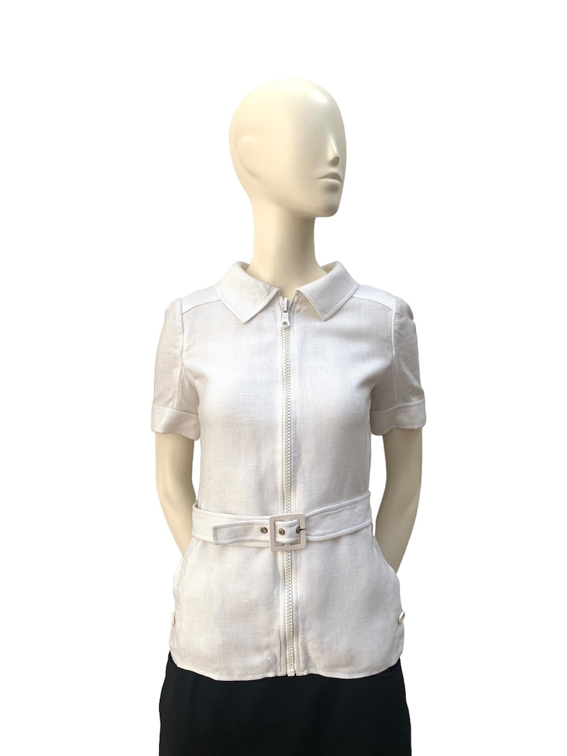 May include: A white linen shirt with a zipper closure and a belt. The shirt has short sleeves and a collared neckline.
