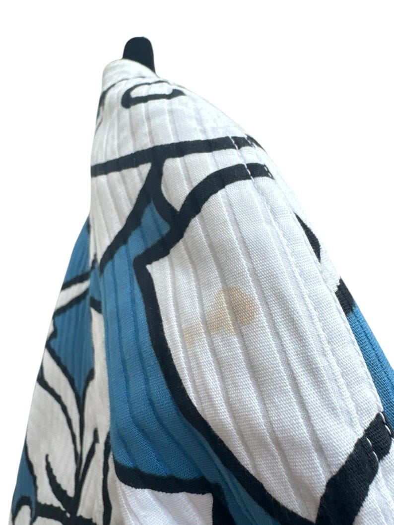 Peut inclure: Gros plan sur un tissu &agrave; motifs blancs et bleus avec des contours noirs. Le tissu a une surface textur&eacute;e et c&ocirc;tel&eacute;e.