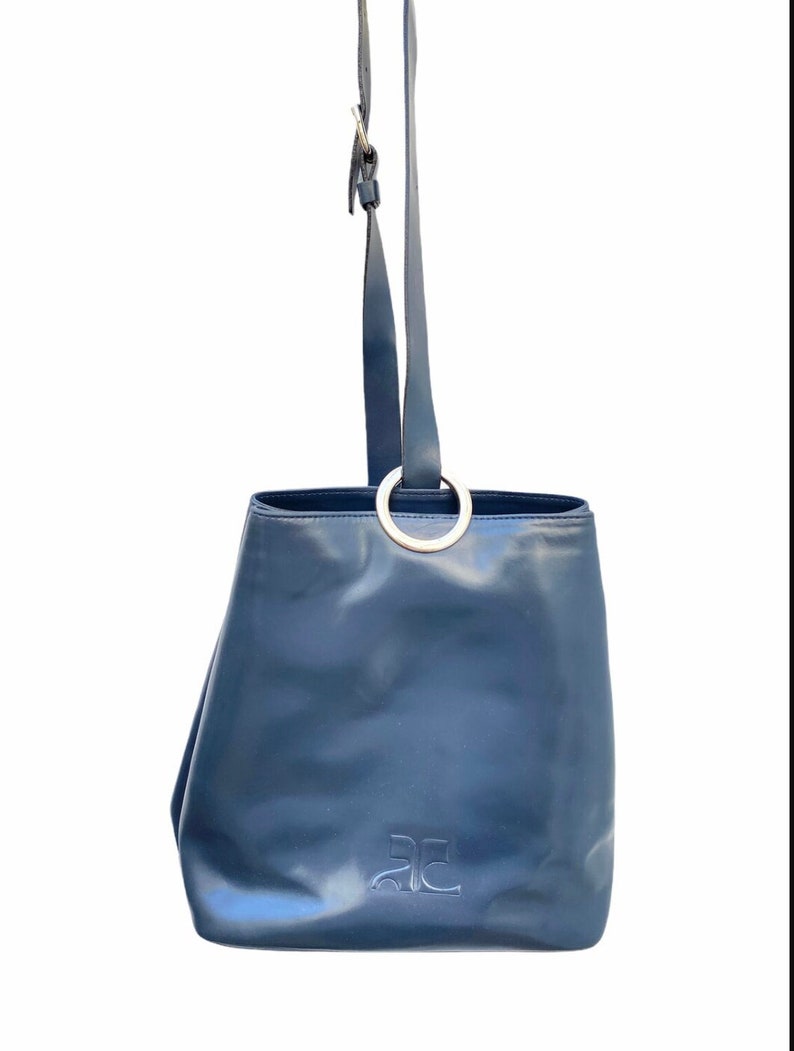 May include: A dark blue leather tote bag with a silver ring handle and the letter 'AC' embossed on the front.