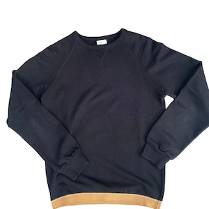 May include: A black long-sleeved sweatshirt with a brown ribbed trim around the bottom. The sweatshirt has a crew neck and raglan sleeves.
