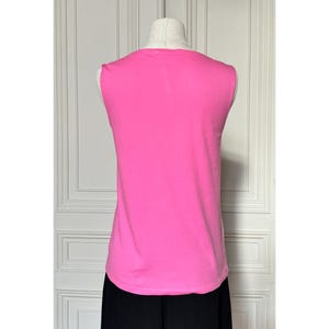 May include: A sleeveless, hot pink top displayed on a mannequin. The top has a rounded neckline and a smooth texture. The bottom portion of the mannequin is wearing black pants. The background is a white door.