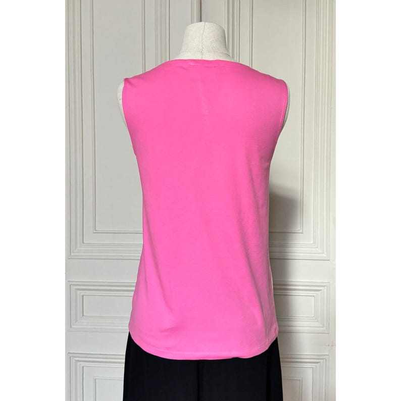 May include: A sleeveless, hot pink top displayed on a mannequin. The top has a rounded neckline and a smooth texture. The bottom portion of the mannequin is wearing black pants. The background is a white door.