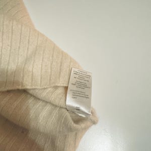 May include: A beige and cream colored knitted sweater with a tag that reads "LA REDOUTE" and includes information about the fabric and care instructions.