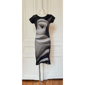 May include: A knee-length short-sleeve dress in black and white, featuring a large, centered graphic print of a rose blossom that spans the entire front of the garment. The dress has a round neckline and a fitted silhouette displayed on a mannequin.