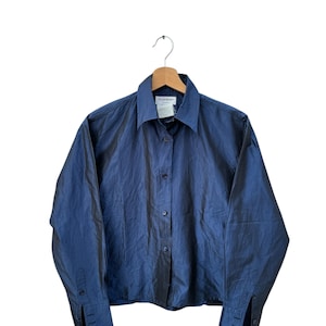 May include: A blue long-sleeved button-up shirt with a YSL label. The shirt is made of a silky material and has a slightly cropped fit.