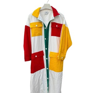 Puede incluir: Una camisa blanca larga con botones y mangas largas. La camisa tiene grandes paneles de color en rojo, amarillo y verde.