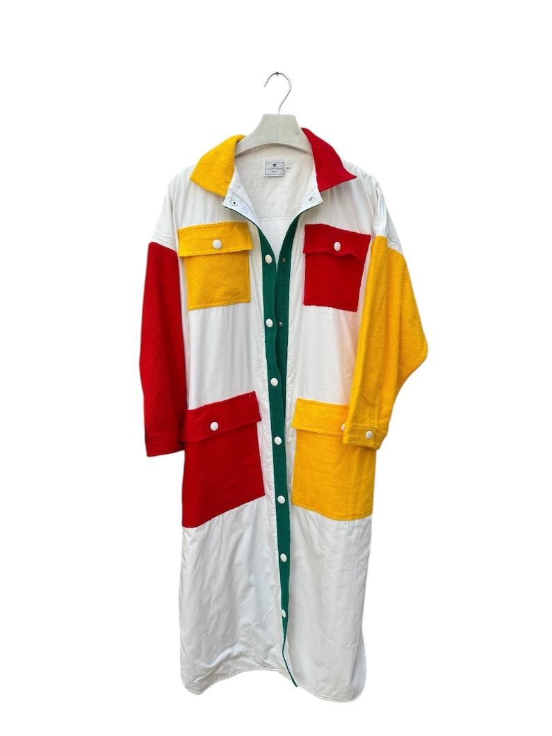 Puede incluir: Una camisa blanca larga con botones y mangas largas. La camisa tiene grandes paneles de color en rojo, amarillo y verde.