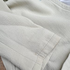 Puede incluir: Un blazer verde claro con tejido texturizado. El blazer tiene un cierre de un solo bot&oacute;n y un corte entallado. El pu&ntilde;o de la manga es visible, mostrando la calidad de las costuras.