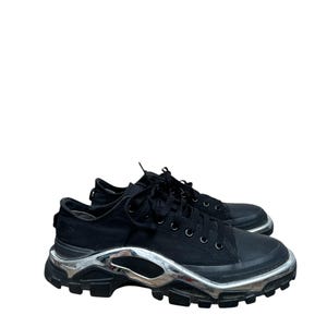 May include: Black canvas sneakers with a silver platform sole. The sneakers have a lace-up closure and a rounded toe.