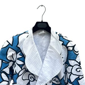 Peut inclure: Une veste blanche avec un motif floral bleu. La veste a une fermeture &agrave; double boutonnage et un grand col.