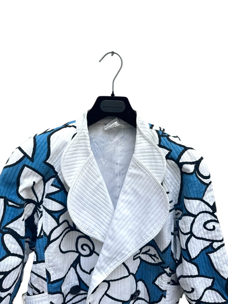 Peut inclure: Une veste blanche avec un motif floral bleu. La veste a une fermeture &agrave; double boutonnage et un grand col.